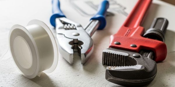 A complete plumbing equipment checklist laid out on a wooden workbench, including wrenches, plungers, and pipe tape