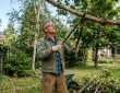 Gardener using long handle loppers to trim thick tree branches in a backyard