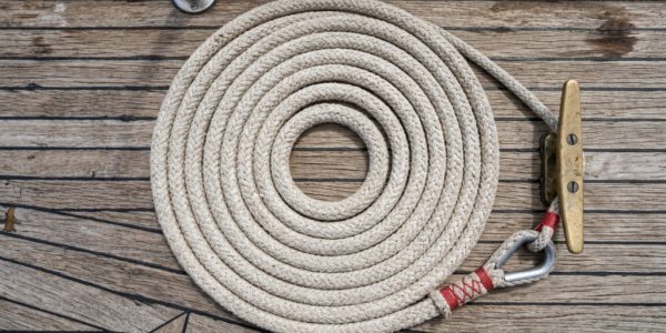 Sailor tying a secure knot in a white anchor rope.