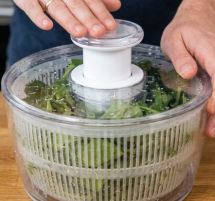 OXO salad spinner on a kitchen counter with fresh greens inside.
