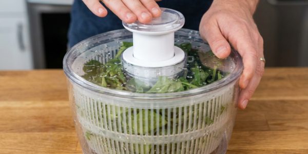 OXO salad spinner on a kitchen counter with fresh greens inside.